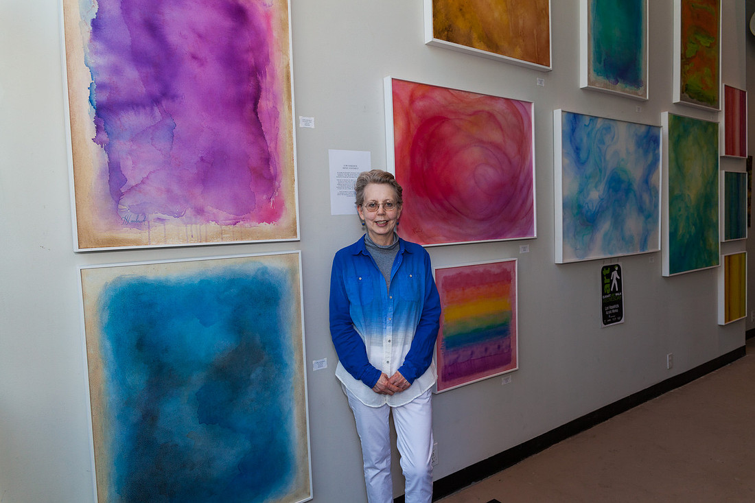 picture of artist standing with her colorfull paintings