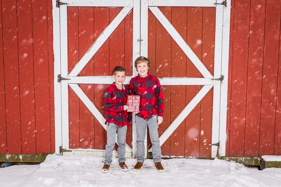picture of  two boys in the snow in front of a red barn