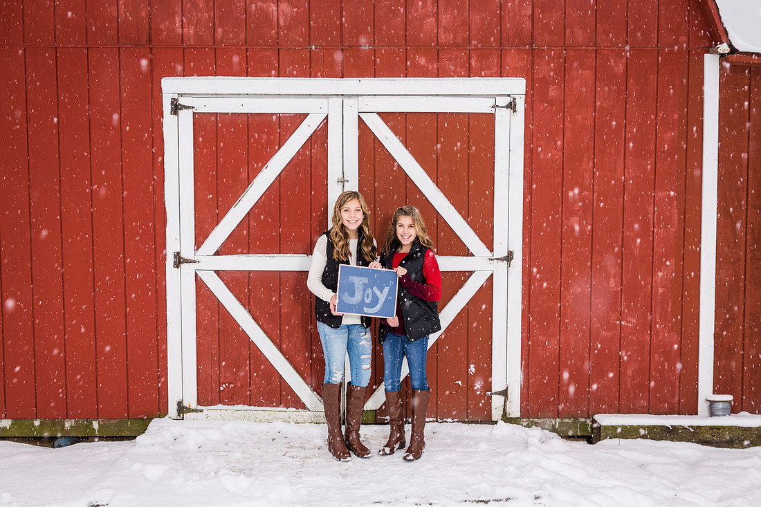 picture of two girls in the snow in front of a red barn