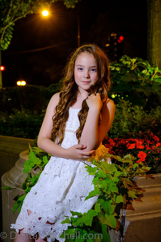 photograph of young girl in white dress next to flowers at night