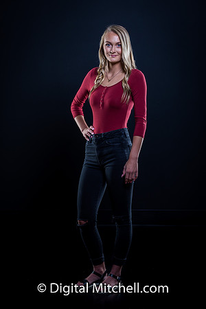 photograph of a high school senior posing in a red top and blue genes on a black background
