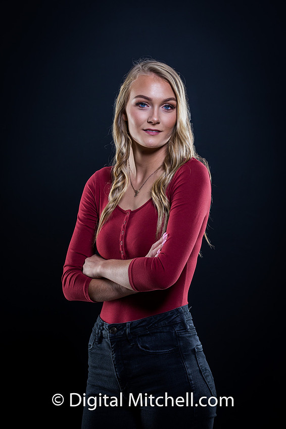 photograph of a high school senior posing in a red top and blue genes on a black background