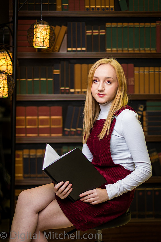young blonde girl sitting in front of a bookshelf